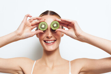 Woman kiwi fruit fresh healthy smiling eyes hands playful wellness concept, young woman holds kiwi halves over eyes on white studio background, showing healthy eating and joy