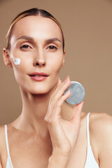 woman face skincare beauty cotton pad closeup portrait, applying gentle cleanser on cheek, calm expression, smooth skin, soft studio light, beige background