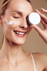 Woman skincare facial cream moisturizer beauty mirror smile treatment spa, close up portrait, woman applies eye cream with fingers, eyes closed, soft studio light