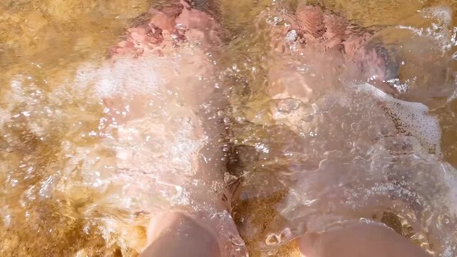Close up shot of feet standing on wet beach sand with gentle ocean waves washing over them.