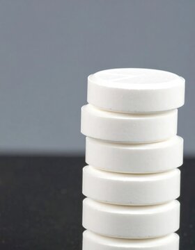 A stack of six white, circular pills is prominently displayed against a muted gray and black background.