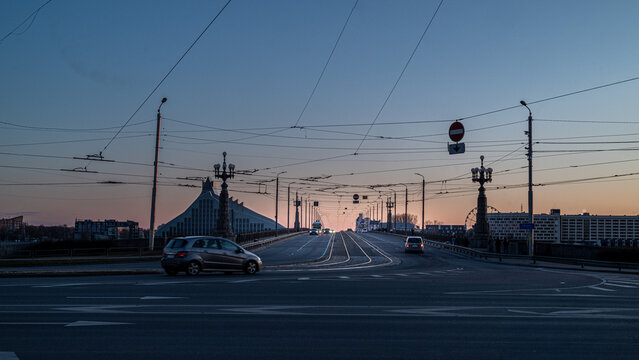 Urban bridge and roadway at dusk with tram lines, city traffic and dramatic evening sky in Riga, Latvia.