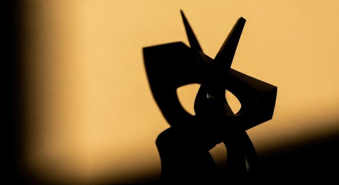 Dramatic black silhouette of a modern abstract sculpture casting a strong shadow against a warm orange-yellow background