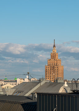 Rooftop view of Riga city skyline with the iconic Academy of Sciences building illuminated by warm evening sunlight under a blue sky with clouds.