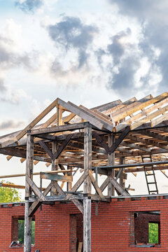 Exposed timber frame above brick foundation, weathered beams and angled trusses under clear sky, scaffolding and tool marks