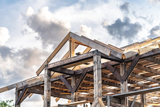 Construction of wooden frame for the roof of cottage in countryside is in progress. Structure stands under cloudy sky