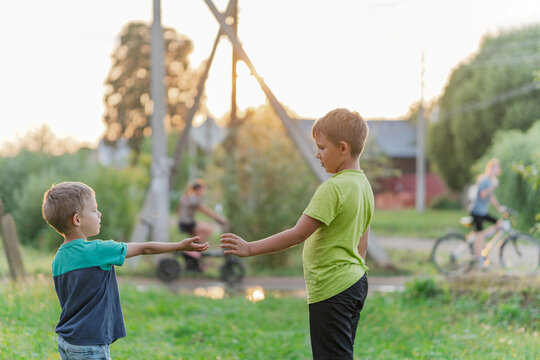 Two boys reaching hands at park, gentle handshake gesture under warm light, cooperative play moment inclusive neighbourhood vibe