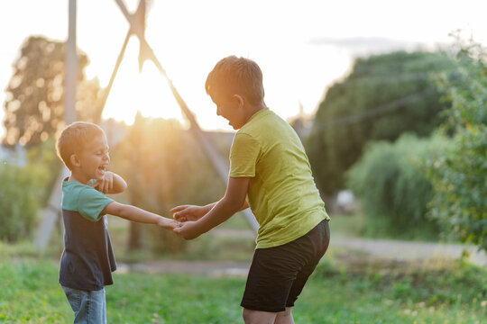 Older boy guiding younger in park play, supportive handhold and encouraging posture, warm backlight with soft bokeh, cooperative moment near climbing structure