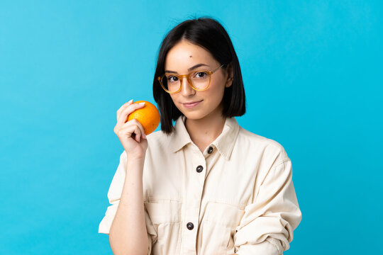 Young caucasian woman isolated on blue background holding an orange
