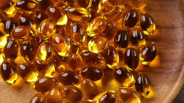 Golden yellow fish oil omega-3 supplement softgel capsules piled on wooden plate, health nutrition vitamin dietary supplement concept