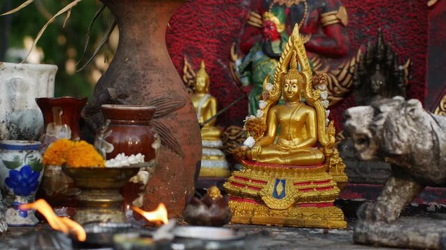 Golden Thai Buddha Statue with Flame Halo Seated on Ornate Base with Candle Flame and Red Offerings