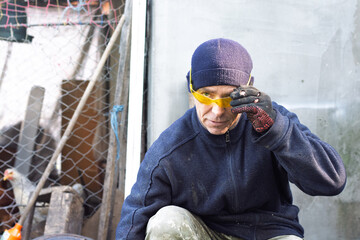 Middle-aged Manual Laborer in Blue Fleece and Yellow Safety Glasses Adjusting Goggles Outdoors © dizfoto1973