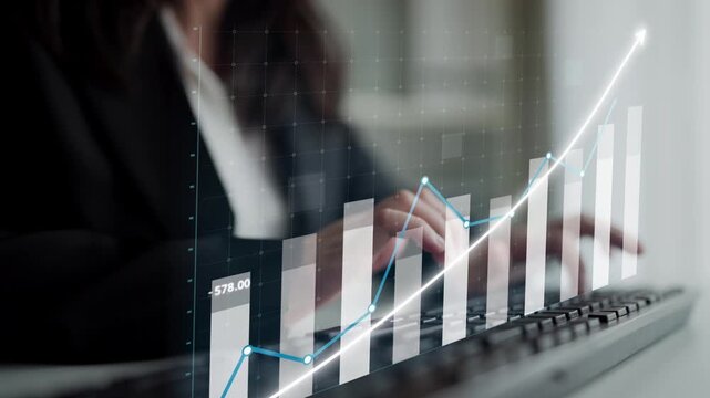 A professional businesswoman engages in financial analysis using a keyboard and observing upward-trending graphs on her screen, illustrating growth and success. Copula
