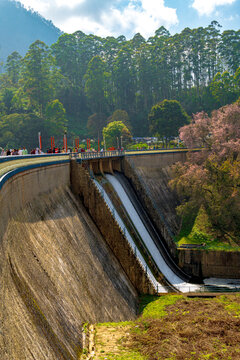 Mattupetty Dam spillway and reservoir in Munnar, Kerala, India - Scenic landscape with flowing water, concrete gravity dam structure, and lush green forest mountains.