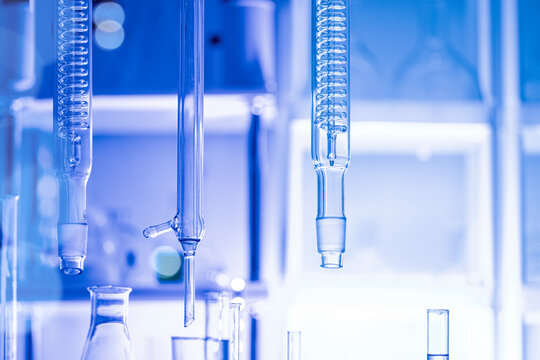 Close-up of laboratory glass condensers and distillation equipment under blue light, blurred background, concept of chemistry research and analytical setup.