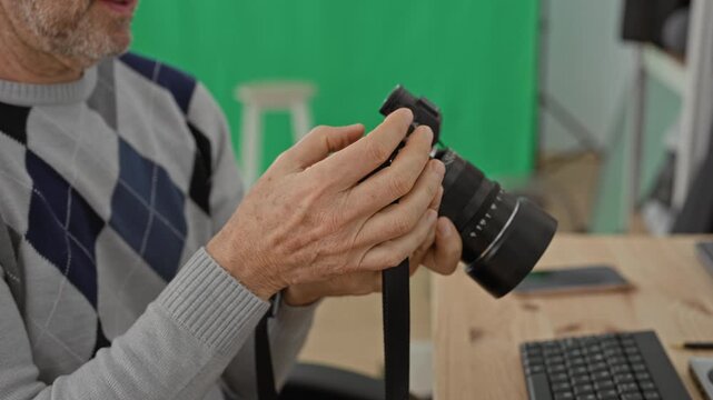 Man photographer adjusts camera with hands in studio green screen set at desk with keyboard and smartphone; quiet concentration.