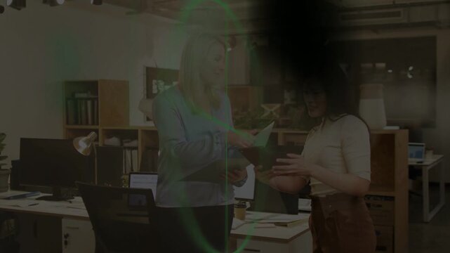 Two women standing in office, tapping device and reviewing report while green overlay clearing view
