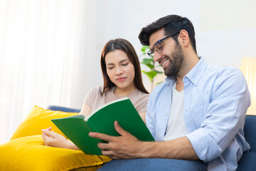 Obraz premium A couple sits reading books together on the sofa in the bright and cozy living room, conveying a happy family lifestyle.
