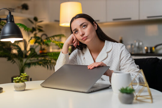 Young woman at night home shuts laptop after work feels burnout wants pause takes breath. Caucasian girl on sofa at table at evening looks tired says enough rubs temples needs break rests eyes closed.
