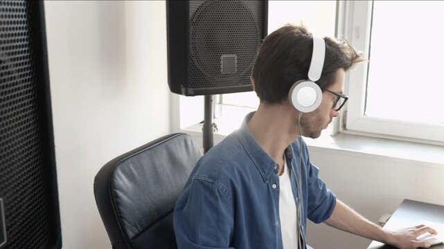 Young man in sound recording studio. Guy listening to music through headphones. Recording music and playing on keyboard like non-professional.