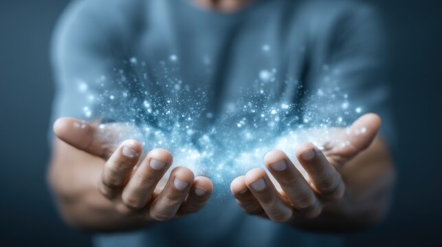 A person holds glowing blue particles of light or energy gently suspended above their open hands against a blurred background, Digital Twin Reality AI technology