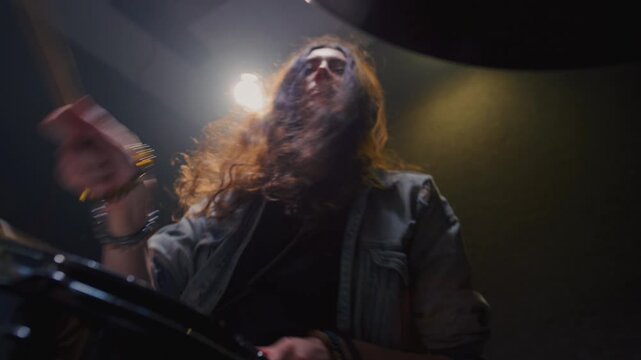 Young female drummer passionately playing a drum kit in a professional rehearsal studio, energetically striking cymbals and drums with drumsticks. Hair flying. Rock Feminist style. Woman power.
