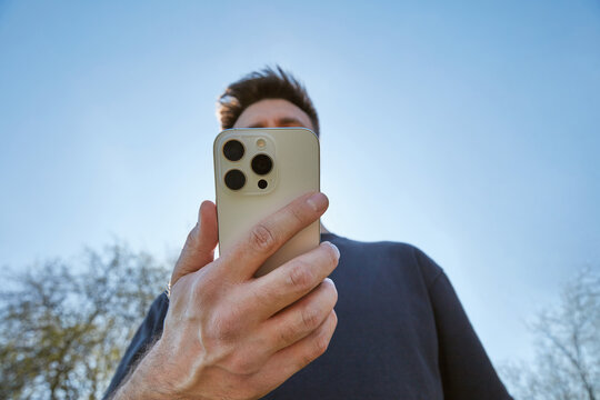 Man Holding Modern White Smartphone Against Blue Sky Outdoors