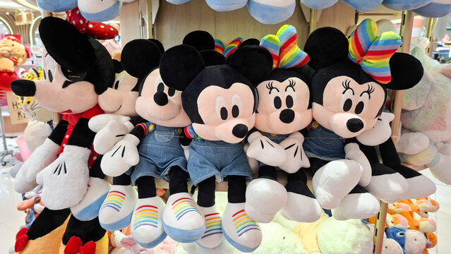 Row of Mickey Mouse and Minnie Mouse plush stuffed animal toys wearing denim overalls and rainbow sneakers displayed on a shelf on May 2, 2026 in Bangkok, Thailand.