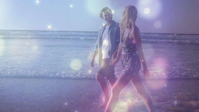 Couple walking along shore, sunlight creating pink bokeh, accenting splashes for travel ad