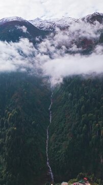 Vertical aerial view of Gelint&uuml;l&uuml; Waterfall in Ayder, Kackar Mountains with snowy peaks and misty clouds