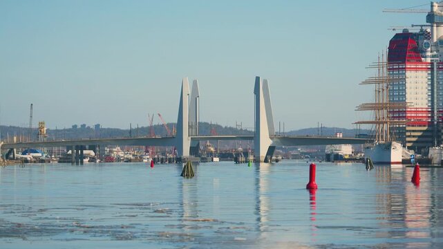 Modern bascule bridge over calm harbor water with ships and city skyline in daylight