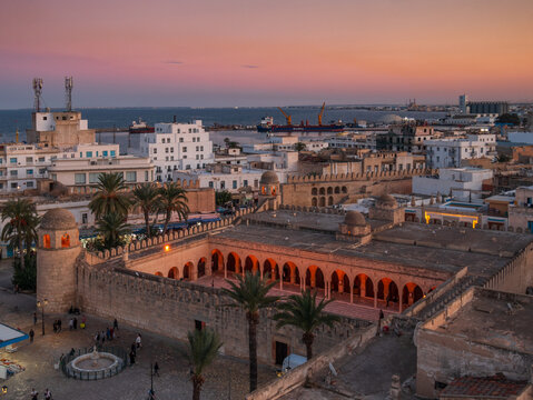 Sunset view over the historic mosque of Sousse, Tunisia, with illuminated stone walls, tower and palm trees, view from above highlighting Islamic architecture and historic atmosphere