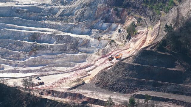Aerial view of a rugged quarry where heavy machinery contrasts against the layered earth, revealing raw textures and tones, Echassieres, Auvergne-Rhone-Alpes, France.