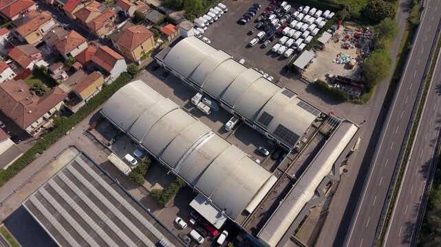 Industrial Warehouses from Above: An aerial view showcases rows of expansive industrial warehouses and a parking lot filled with vehicles, situated next to a residential area and a road.