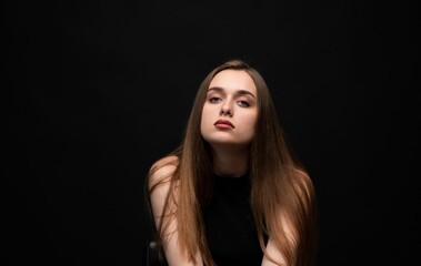 Fototapeta premium Young woman with long brown hair posing confidently against a black background, looking directly at camera