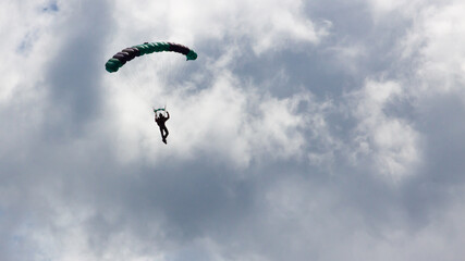 Single parachutist descending under a colorful parachute against a cloudy sky. Extreme sport adventure in mid-air. © David