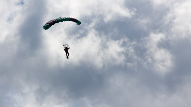 Single parachutist descending under a colorful parachute against a cloudy sky. Extreme sport adventure in mid-air.
