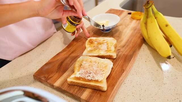 Woman spreading vegemite on buttered toast for breakfast in modern kitchen environment.