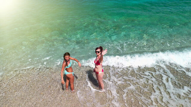 Mother and daughter standing on beach shore with small waves in aerial perspective