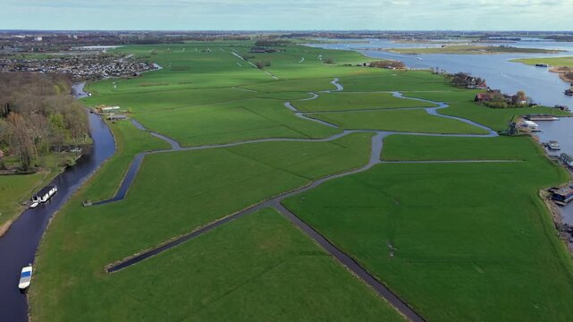 Panoramic aerial view of lush green Dutch polders and meadows crisscrossed by canals. A classic Netherlands landscape featuring a traditional windmill, waterways, and rural countryside scenery.