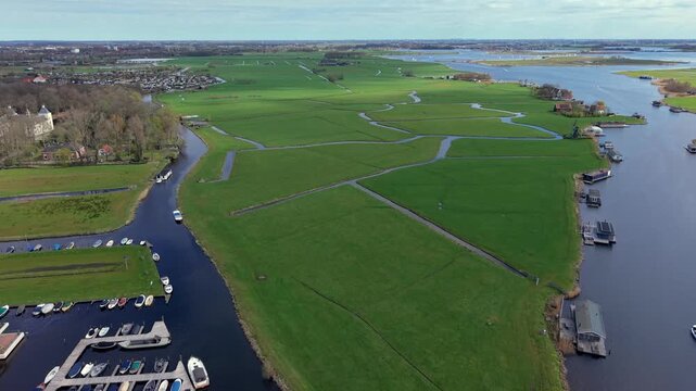 Panoramic aerial view of lush green Dutch polders and meadows crisscrossed by canals. A classic Netherlands landscape featuring a traditional windmill, waterways, and rural countryside scenery.