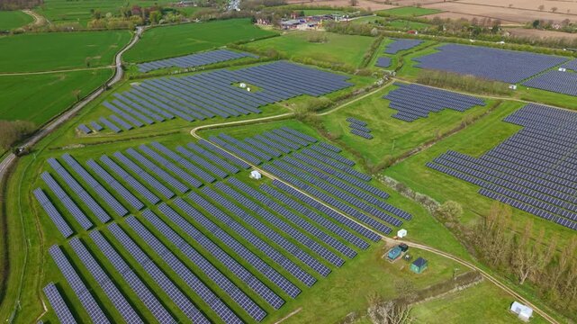 Wide drone shot of renewable energy solar panels integrated into British farmland, sunny photovoltaic energy generation UK 4k