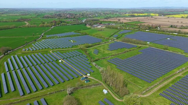 Wide drone shot of renewable energy solar panels integrated into British farmland, sunny photovoltaic energy generation UK 4k