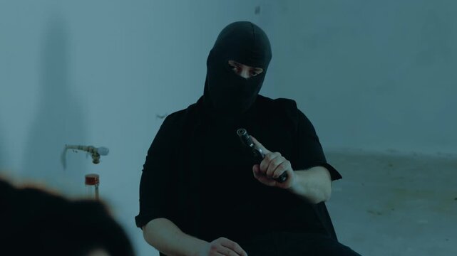 Kidnapper threatening a woman with a gun in the basement. Male robber is pouring alcohol into a glass. Kidnaping, crime, violence concept. Slow motion