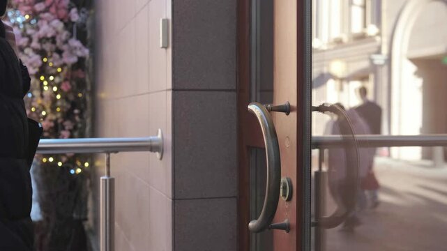 Female hand pulling metal door handle. Glass entrance door is closed and locked. Urban street access denied scenario for business or shop.