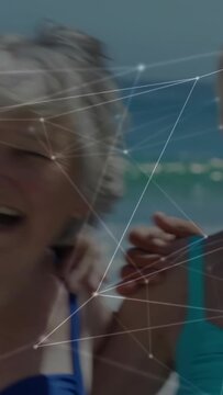 Vertical video: Camera panning, seniors laughing and raising arms on beach for travel, overlaying
