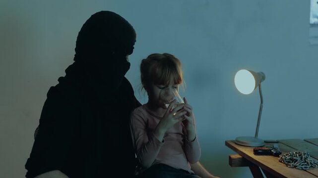 Kidnapper holding the girl hostage in his arms while giving a glass of water for her. Copy space. Kidnapping. Child abduction concept. Slow motion