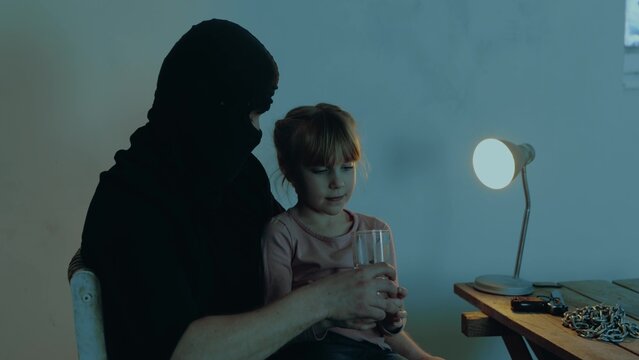 Kidnapper holding the girl hostage in his arms while giving a glass of water for her. Copy space. Kidnapping. Child abduction concept.