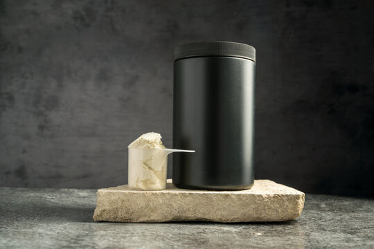 Protein whey powder black plastic tube, on dark background with scoop.