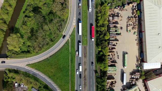 Top down aerial view of a busy main road with moving traffic parallel to a calm canal with a traditional narrowboat in Burton-on-Trent UK